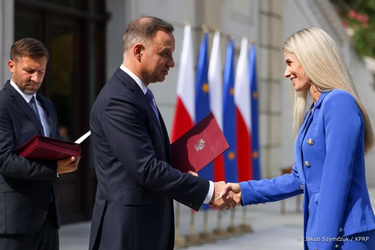 dwóch mężczyzn i kobieta, jeden z mężczyzn (Prezydent RP Andrzej Duda) wręcza kobiecie dokument