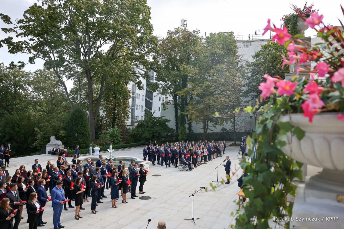 mężczyzna (Prezydent RP Andrzej Duda) przemawia przez mikrofon do grupy osób stojących na placu w Pałacu Prezydenckim