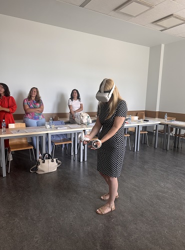 Kobieta w goglach VR w sali wykładowej KSSiP , w rękach trzyma kontrolery. 