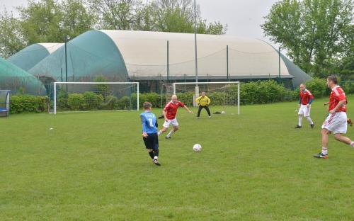 Zdjęcie nr 6: czterech mężczyzn biegających po boisku piłkarskim za piłką do piłki nożnej oraz jeden mężczyzna stojący na bramce