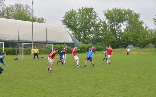 Zdjęcie nr 7: dziewięciu mężczyzn biegających po boisku piłkarskim za piłką do piłki nożnej oraz jeden mężczyzna stojący na bramce, w oddali kolejna osoba, która przygląda się grze