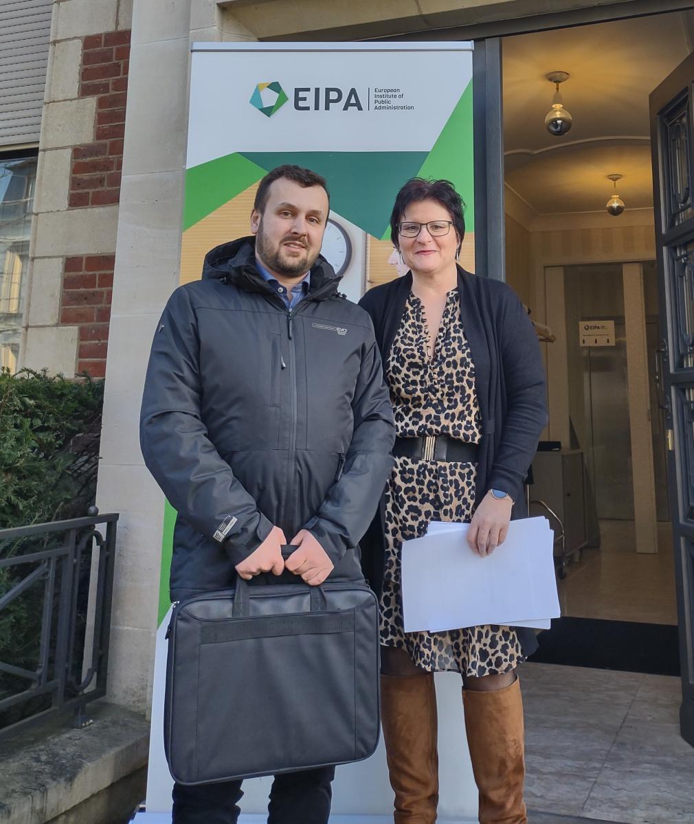 Przedstawiciel EIPA i KSSIP- kobieta i mężczyzna stoją na tle białozielonego baneru z logo gospodarza projektu - Europejskiego Instytutu Administracji Publicznej.