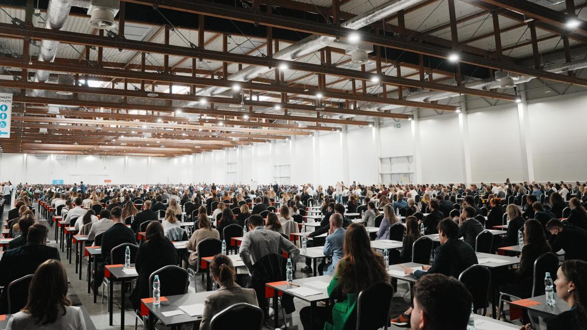 na zdjęciu widać salę, na krzesłach siedzą mężczyźni i kobiety, którzy są uczestnikami konkursu naboru na aplikację.